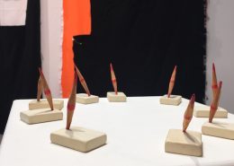 3D work comprising a circle of rubbers inset with pencils sharpened at both ends by Suely Farhi mounted on a plinth, entitled Totems , behind which is Jacqueline Belotti's black and red Fabrics