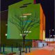 Oil painting by Daniel Preece of a city scape at night with green light on the side of a modern building