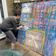 Artist Sandra Beccarelli creating artwork outside- drilling holes in a large colourful abstract canvas during lockdown